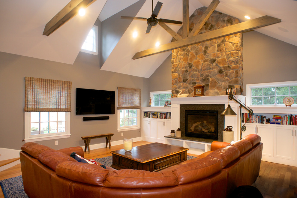 Cette image montre une salle de séjour marine de taille moyenne et ouverte avec un mur gris, un sol en bois brun, une cheminée standard, un manteau de cheminée en bois, un téléviseur fixé au mur et un plafond voûté.