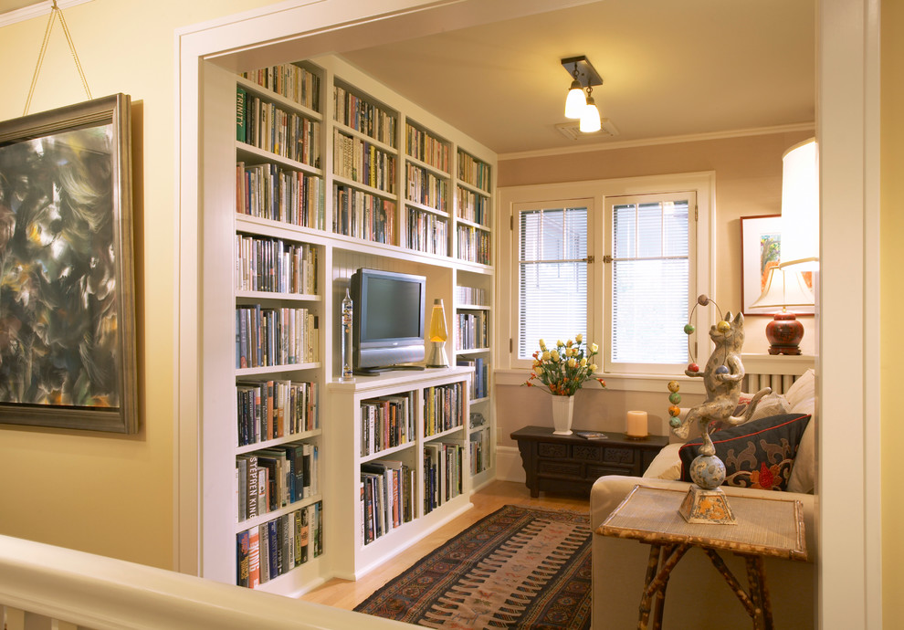Diseño de sala de estar con biblioteca cerrada de estilo americano sin chimenea con paredes amarillas, suelo de madera clara, televisor independiente y alfombra