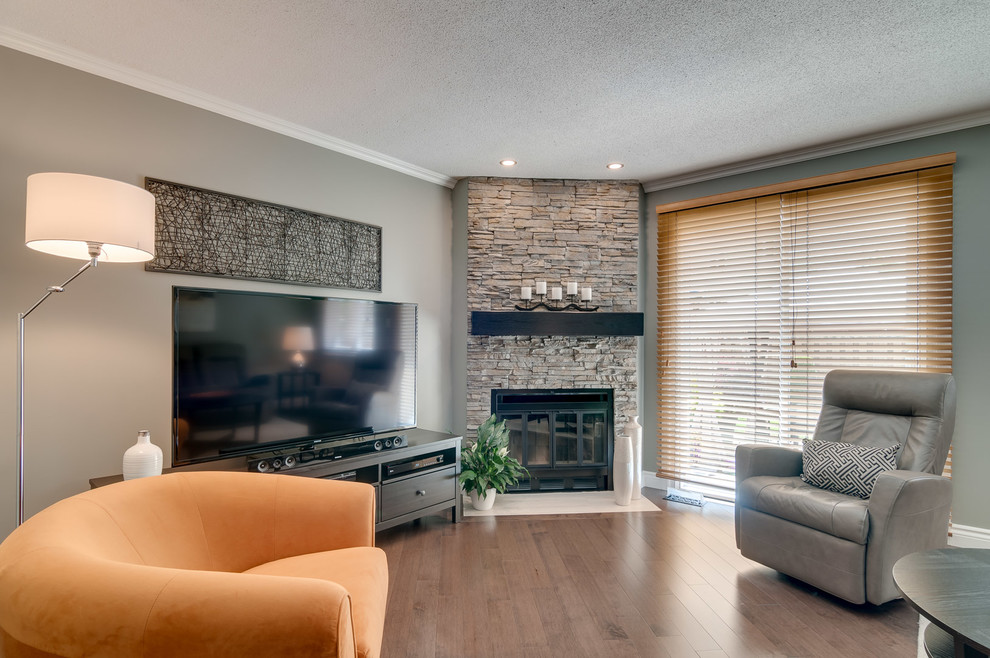 Family room - mid-sized contemporary enclosed medium tone wood floor family room idea in Ottawa with multicolored walls, a corner fireplace, a stone fireplace and a tv stand
