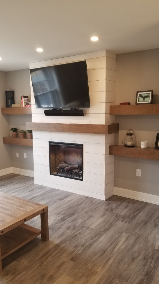 This is an example of a medium sized modern open plan games room in Other with grey walls, vinyl flooring, a standard fireplace, a wooden fireplace surround, a wall mounted tv and grey floors.
