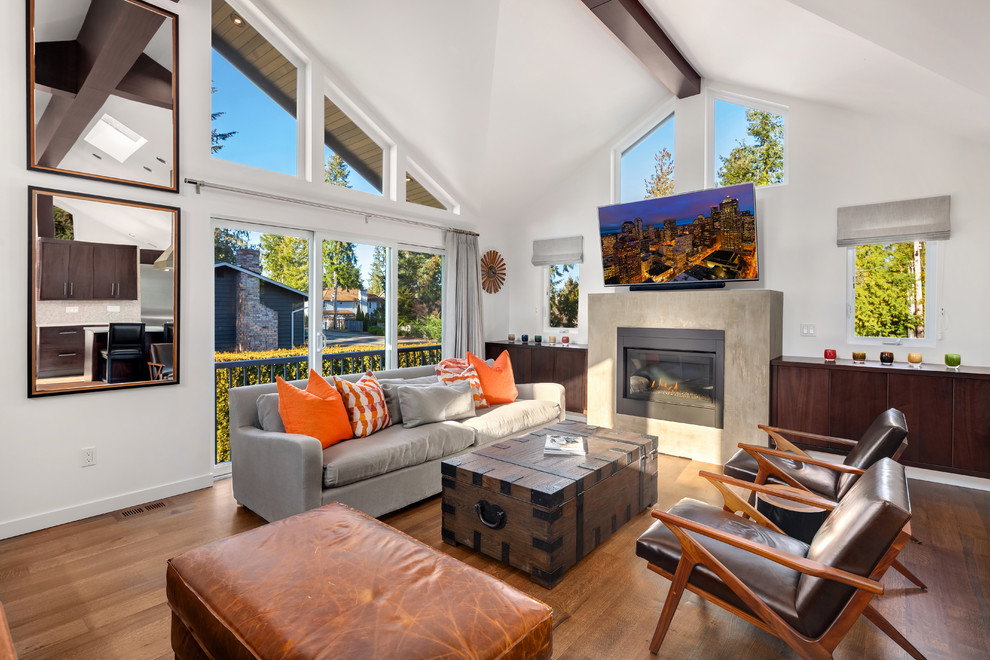 This is an example of a large classic open plan games room in Seattle with white walls, a standard fireplace, a plastered fireplace surround, a wall mounted tv, brown floors and medium hardwood flooring.