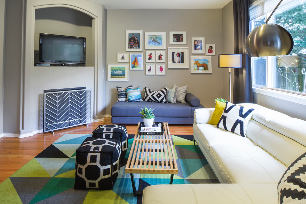 Imagen de sala de estar abierta minimalista de tamaño medio con paredes grises, suelo de madera en tonos medios, chimenea de esquina, marco de chimenea de yeso y televisor en una esquina