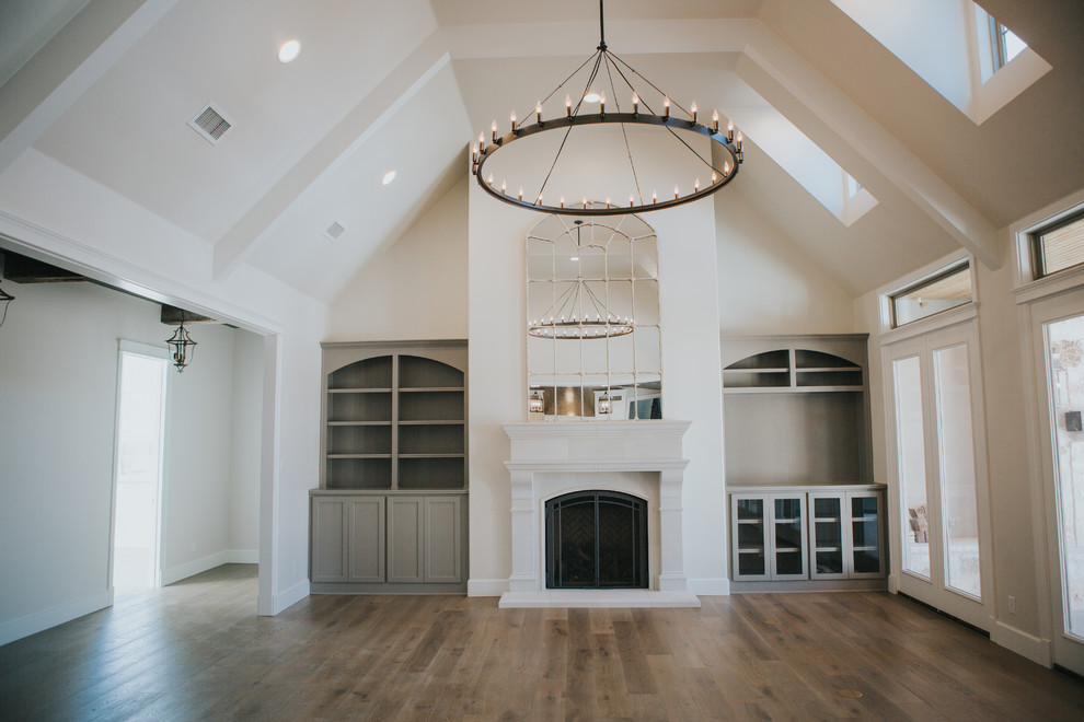 Modelo de sala de estar abierta tradicional renovada grande con paredes blancas, suelo de madera en tonos medios, todas las chimeneas, marco de chimenea de piedra y pared multimedia