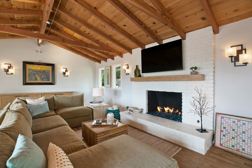 Réalisation d'une salle de séjour champêtre de taille moyenne avec un mur blanc, un sol en bois brun, une cheminée standard, un manteau de cheminée en brique, un téléviseur fixé au mur et un sol marron.