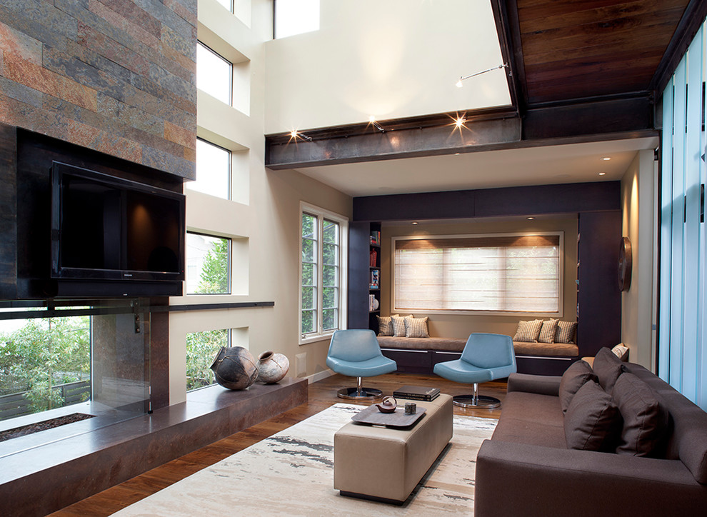 Ejemplo de sala de estar abierta contemporánea grande con paredes beige, televisor colgado en la pared, suelo de madera oscura, chimenea de doble cara y marco de chimenea de yeso