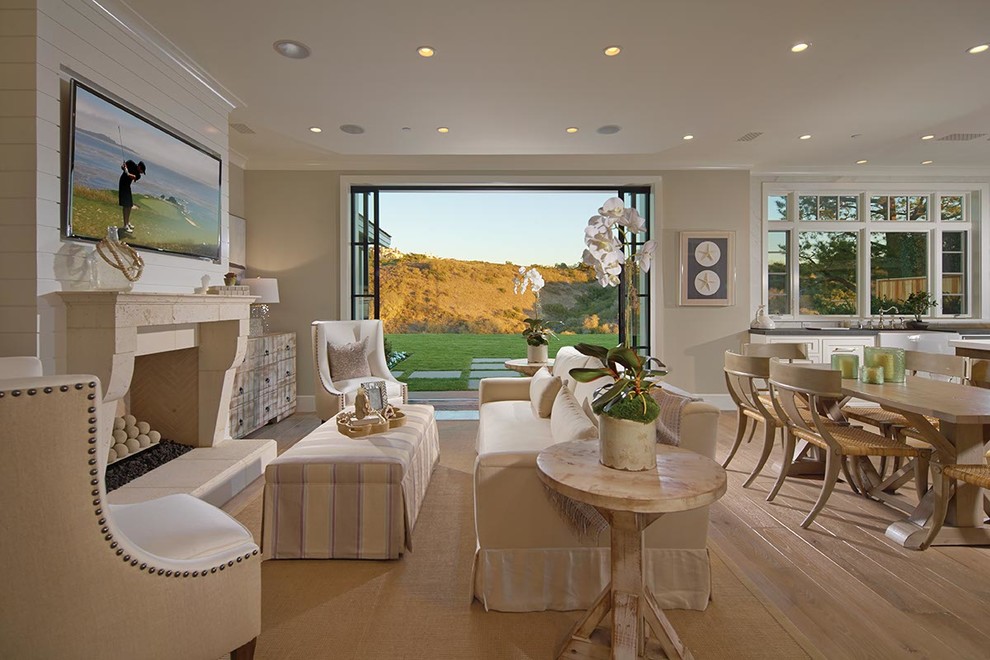 Modelo de sala de estar abierta marinera con paredes beige, suelo de madera clara y televisor colgado en la pared
