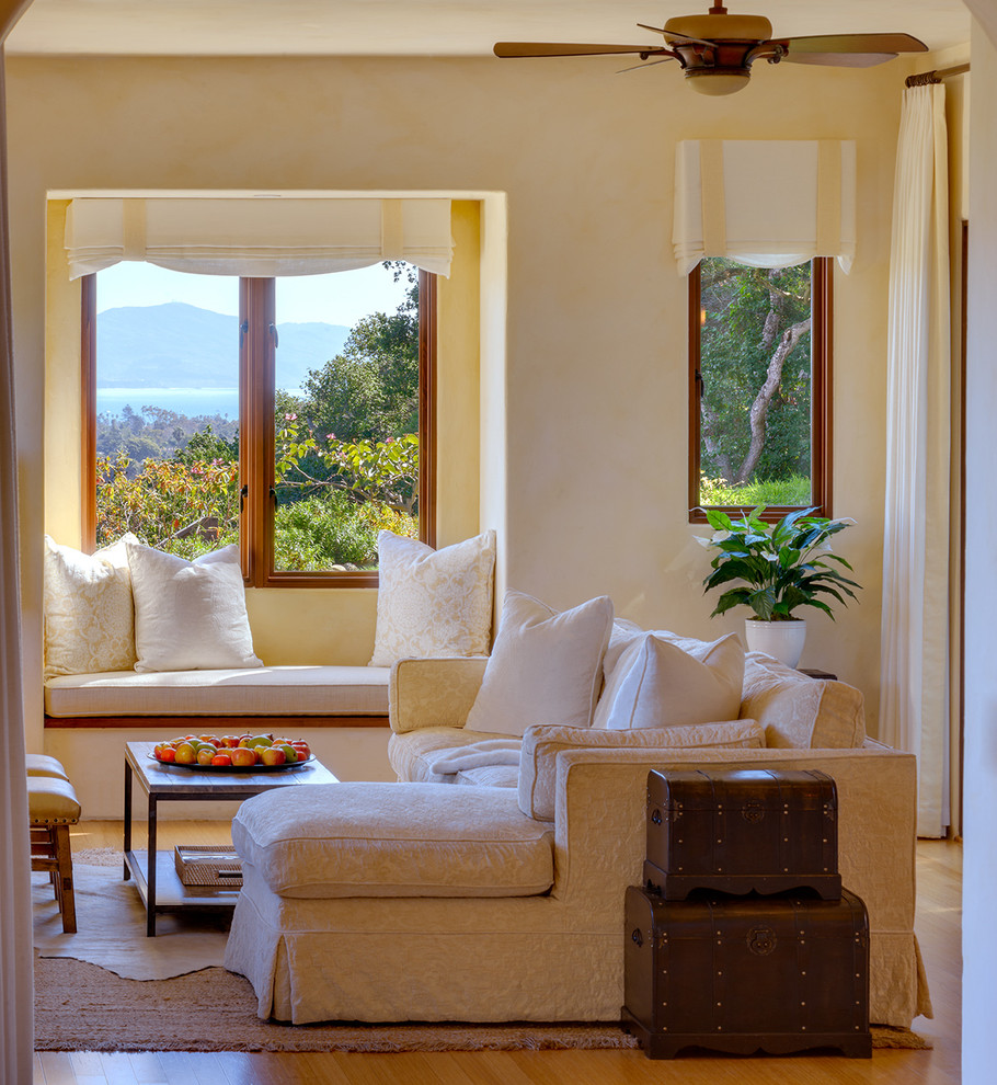 Ejemplo de sala de estar mediterránea de tamaño medio con paredes amarillas, suelo de bambú, todas las chimeneas, marco de chimenea de piedra y televisor colgado en la pared