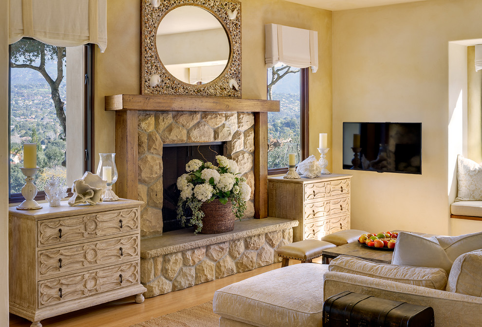 На фото: гостиная комната среднего размера в средиземноморском стиле с желтыми стенами, полом из бамбука, стандартным камином, фасадом камина из камня и телевизором на стене