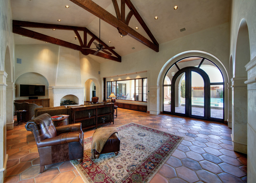This is an example of a mediterranean open plan games room in Austin with beige walls, terracotta flooring, a standard fireplace and a wall mounted tv.