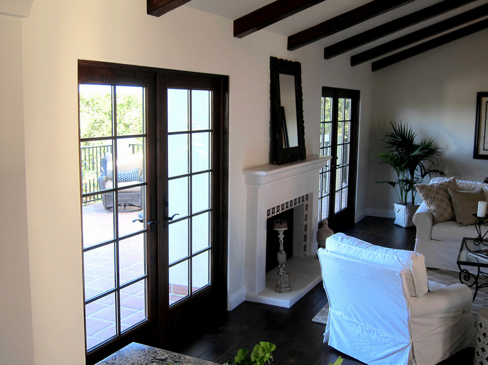 Imagen de sala de estar abierta mediterránea de tamaño medio con paredes blancas, suelo de madera oscura, todas las chimeneas, marco de chimenea de hormigón y suelo marrón