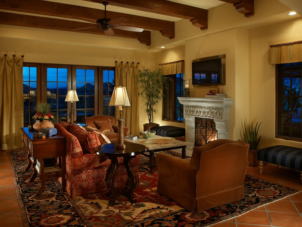 Mittelgroßes, Offenes Mediterranes Wohnzimmer mit gelber Wandfarbe, Terrakottaboden, Kamin, Kaminumrandung aus Stein und TV-Wand in Phoenix