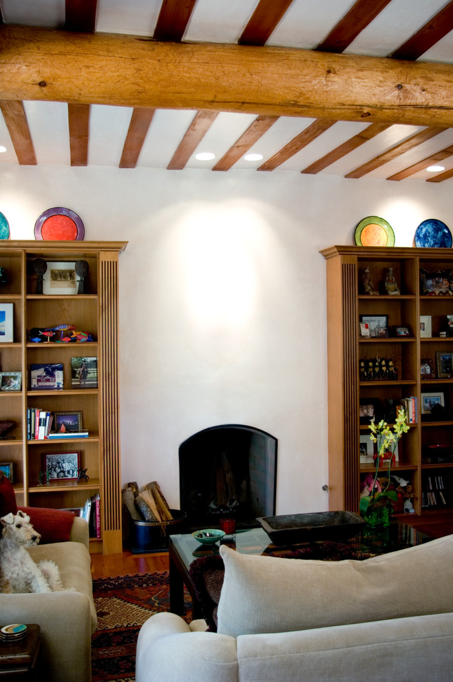 Imagen de sala de estar con biblioteca abierta de estilo americano grande sin televisor con paredes blancas, suelo de madera en tonos medios, todas las chimeneas y marco de chimenea de yeso