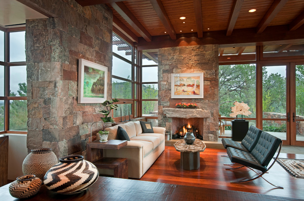 This is an example of a large open plan games room in Albuquerque with multi-coloured walls, dark hardwood flooring, a standard fireplace, a stone fireplace surround, no tv and brown floors.
