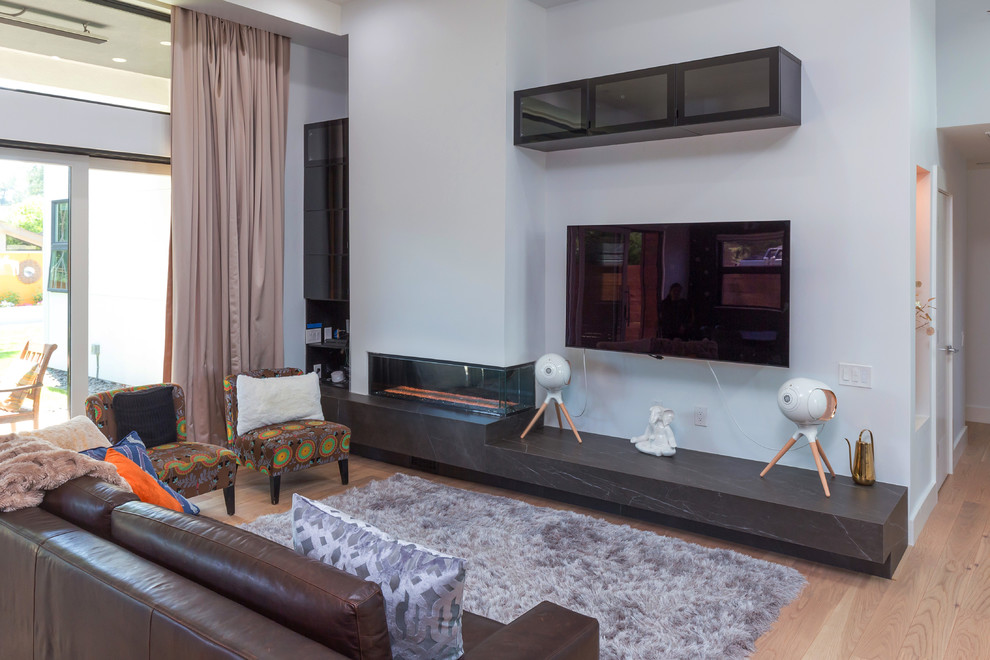 Ejemplo de sala de estar abierta contemporánea pequeña con paredes blancas, suelo de madera clara, chimenea de doble cara, televisor colgado en la pared, suelo beige y marco de chimenea de yeso