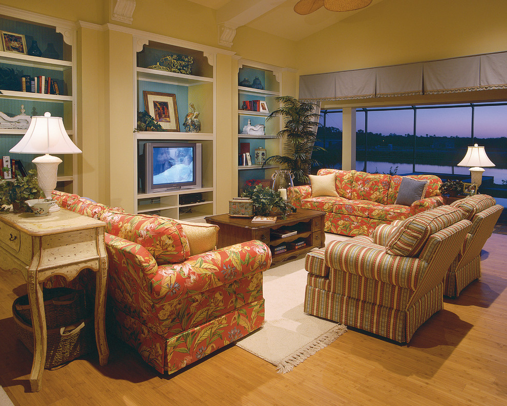 Großes, Offenes Landhaus Wohnzimmer ohne Kamin mit gelber Wandfarbe, braunem Holzboden und freistehendem TV in Miami