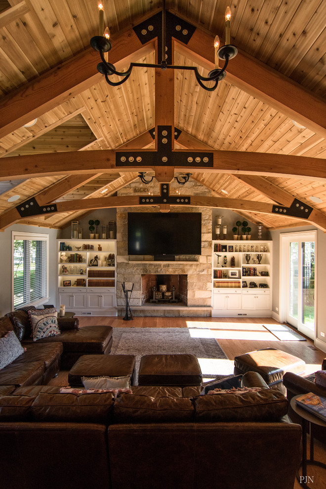 Inspiration for a large traditional open plan games room in Chicago with grey walls, medium hardwood flooring, a standard fireplace, a stone fireplace surround, a wall mounted tv and brown floors.