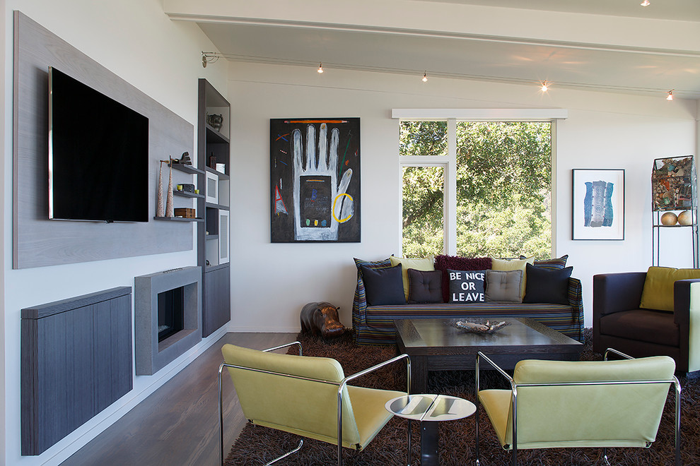 Imagen de sala de estar abierta actual grande con paredes blancas, suelo de madera en tonos medios, chimenea lineal, marco de chimenea de hormigón y pared multimedia