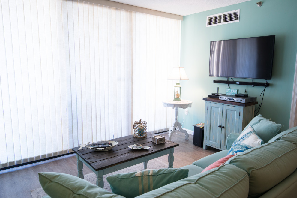 На фото: открытая гостиная комната среднего размера в морском стиле с полом из ламината и телевизором на стене с