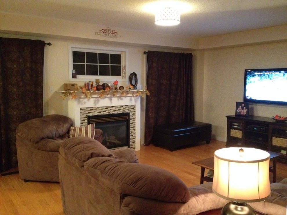 This is an example of a medium sized classic open plan games room in Toronto with beige walls, light hardwood flooring, a standard fireplace, a tiled fireplace surround, a wall mounted tv and beige floors.