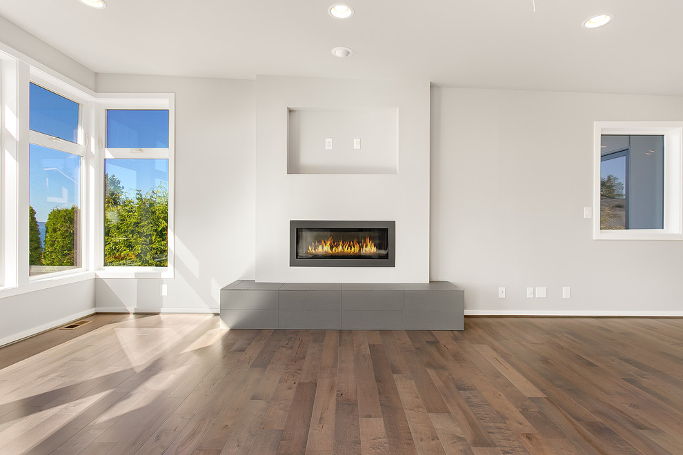 Réalisation d'une grande salle de séjour minimaliste ouverte avec un mur gris, un sol en bois brun, une cheminée standard, un manteau de cheminée en carrelage et un téléviseur fixé au mur.