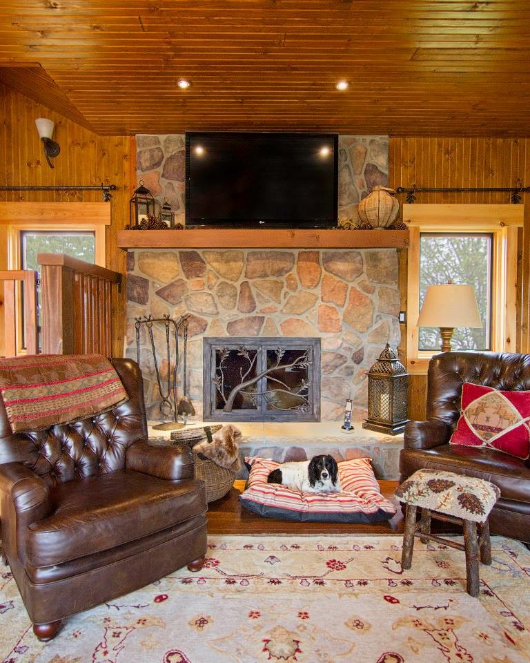Diseño de sala de estar abierta rural grande con suelo de madera en tonos medios, todas las chimeneas, marco de chimenea de piedra, televisor colgado en la pared y paredes grises