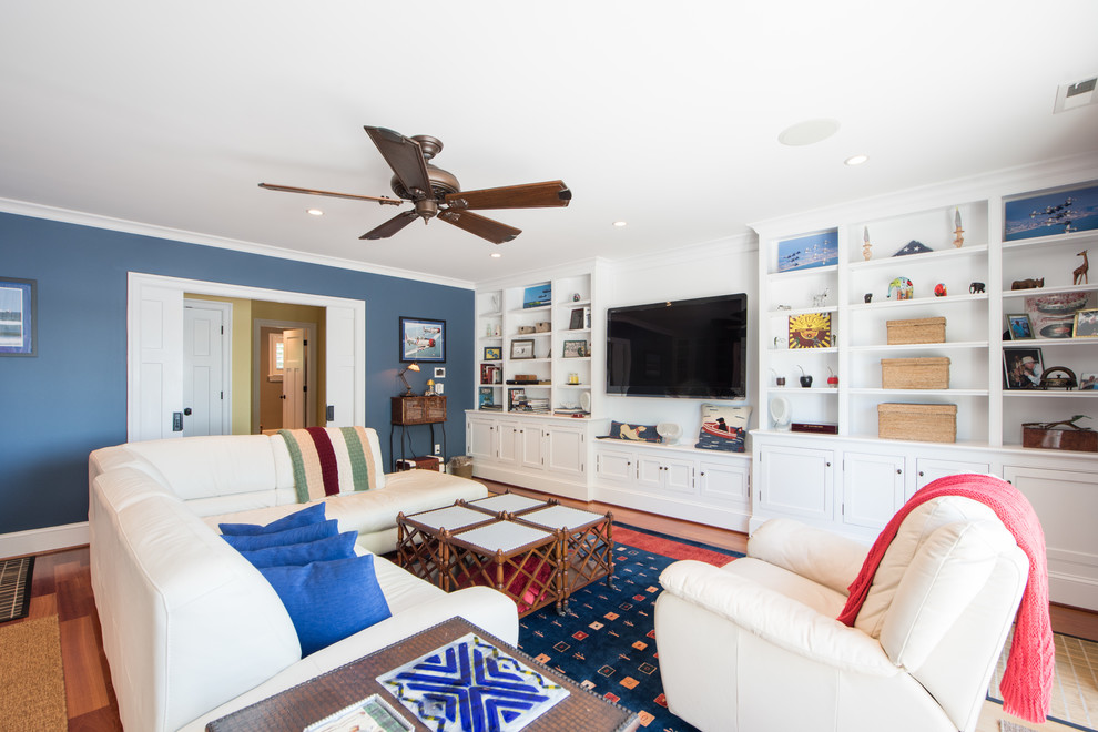 На фото: большая изолированная гостиная комната в стиле кантри с синими стенами, паркетным полом среднего тона и телевизором на стене без камина