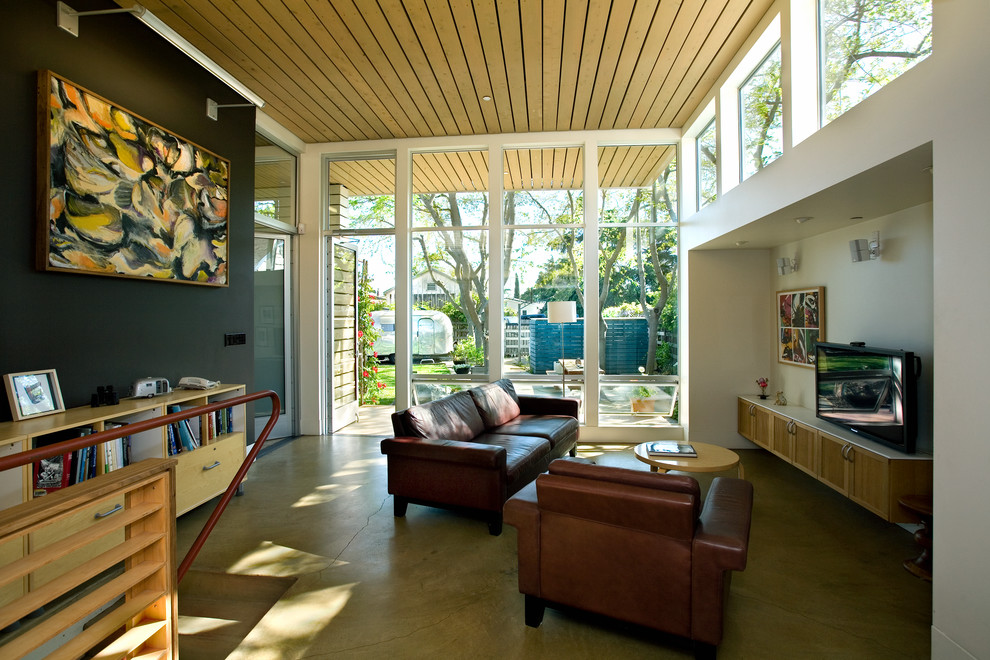 Bild på ett funkis allrum med öppen planlösning, med svarta väggar, betonggolv, en fristående TV och grönt golv