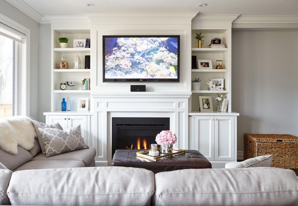 На фото: открытая гостиная комната среднего размера в стиле неоклассика (современная классика) с серыми стенами, паркетным полом среднего тона, стандартным камином, фасадом камина из камня и телевизором на стене