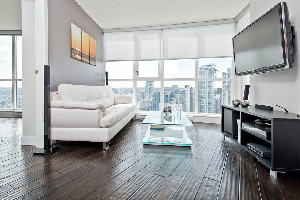 Diseño de sala de estar actual de tamaño medio sin chimenea con suelo de madera oscura, paredes grises y televisor colgado en la pared