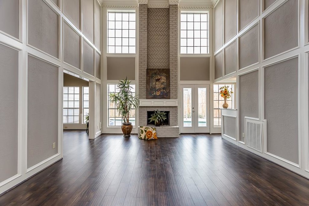 Imagen de sala de estar clásica grande con paredes grises, suelo de madera en tonos medios y marco de chimenea de ladrillo