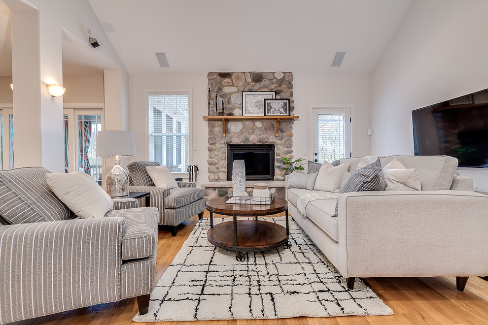 Inspiration for a country open plan games room in Columbus with white walls, light hardwood flooring, a standard fireplace, a stone fireplace surround, a wall mounted tv and brown floors.