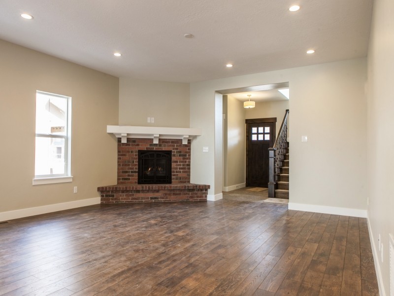 Imagen de sala de estar abierta de estilo americano grande con paredes beige, suelo de madera en tonos medios, chimenea de esquina y marco de chimenea de ladrillo