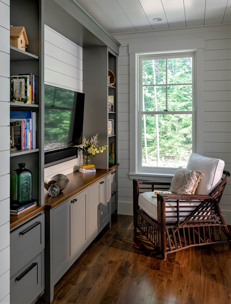 Imagen de sala de estar con biblioteca cerrada de estilo americano pequeña con paredes blancas, suelo de madera oscura, pared multimedia y suelo marrón