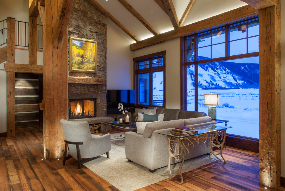 Cette photo montre une salle de séjour montagne ouverte avec un mur blanc, un sol en bois brun, une cheminée standard, un manteau de cheminée en pierre, un téléviseur indépendant et un sol marron.