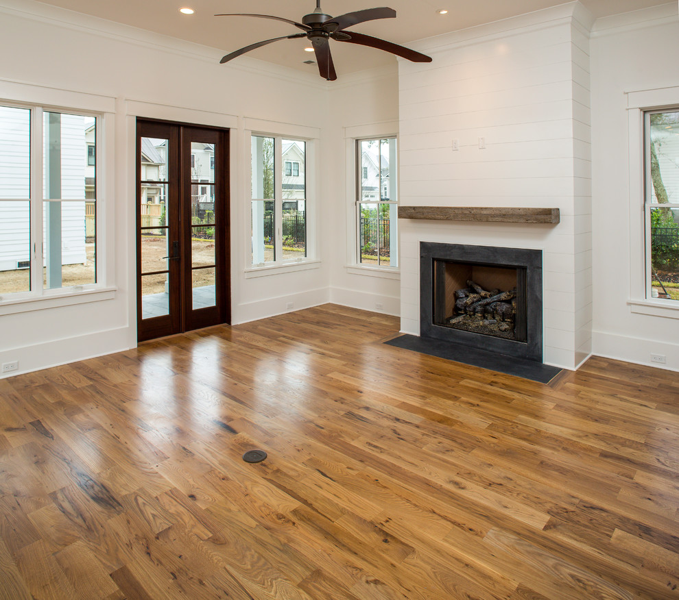 Mittelgroßes, Offenes Modernes Wohnzimmer mit weißer Wandfarbe, braunem Holzboden, Kamin, Kaminumrandung aus Stein und TV-Wand in Charleston