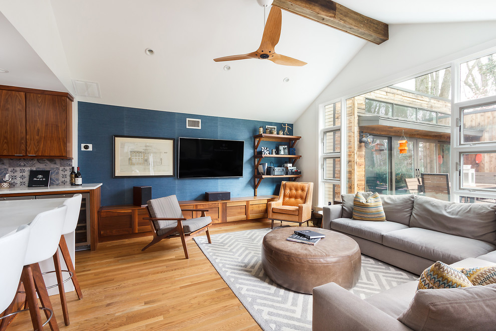 Modelo de sala de estar abierta contemporánea sin chimenea con paredes azules, suelo de madera en tonos medios, televisor colgado en la pared y alfombra