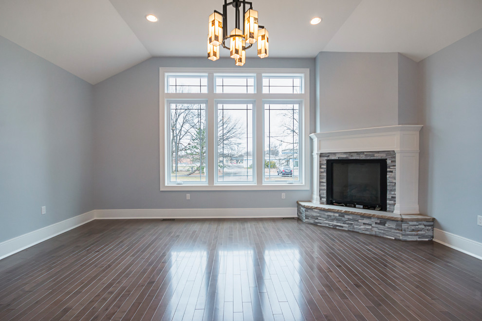 Imagen de sala de estar abierta de estilo americano de tamaño medio con paredes grises, suelo laminado, chimenea de esquina, marco de chimenea de piedra y suelo marrón