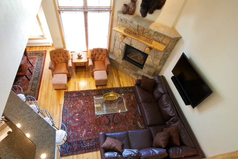 Cette image montre une grande salle de séjour traditionnelle ouverte avec un mur beige, parquet clair, une cheminée standard, un manteau de cheminée en pierre, un téléviseur fixé au mur et un sol marron.