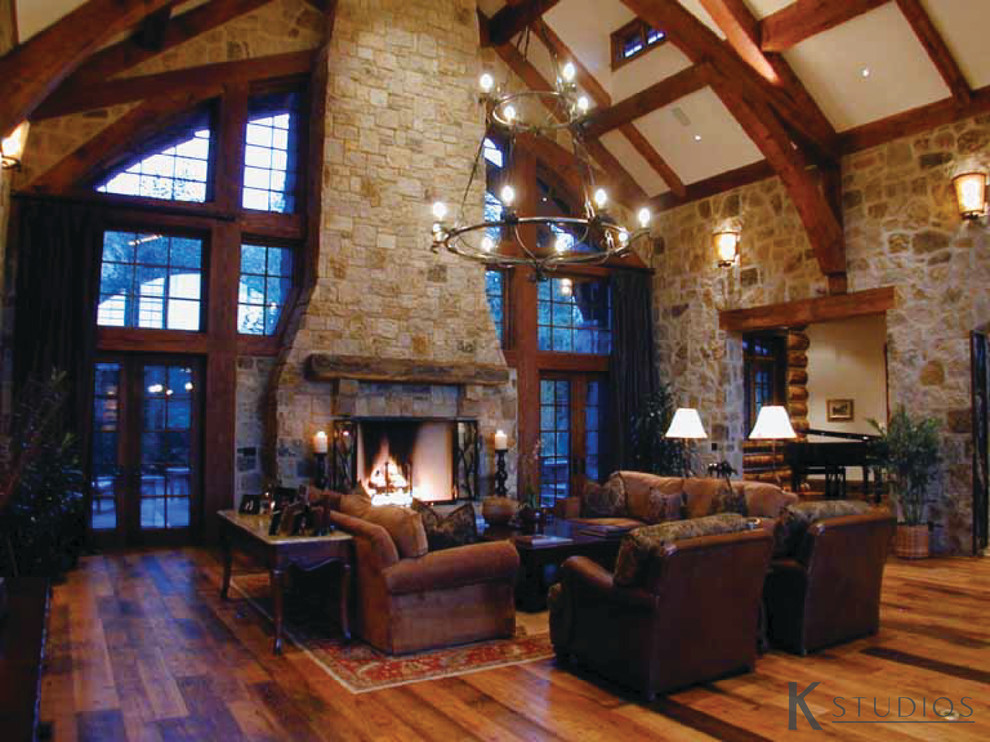 Inspiration pour une très grande salle de séjour chalet ouverte avec un sol en bois brun, une cheminée standard et un manteau de cheminée en pierre.