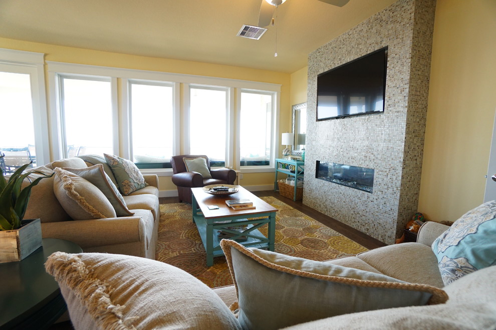 Ejemplo de sala de estar abierta costera de tamaño medio con paredes amarillas, marco de chimenea de baldosas y/o azulejos, televisor colgado en la pared, suelo de madera oscura y chimenea lineal
