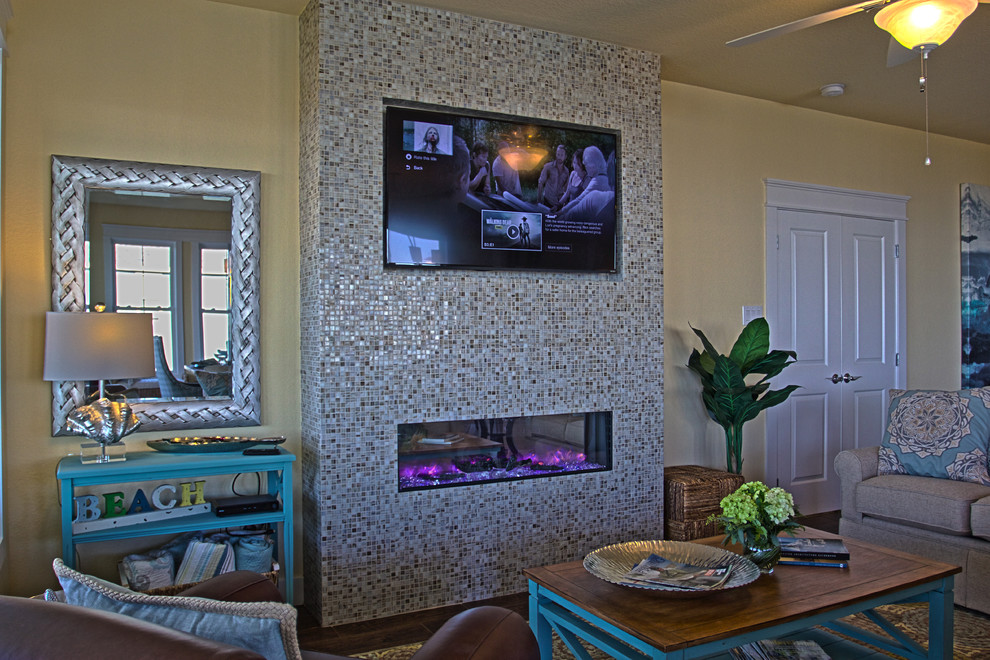 Modelo de sala de estar abierta costera de tamaño medio con paredes amarillas, marco de chimenea de baldosas y/o azulejos, televisor colgado en la pared, suelo de madera oscura y chimenea lineal