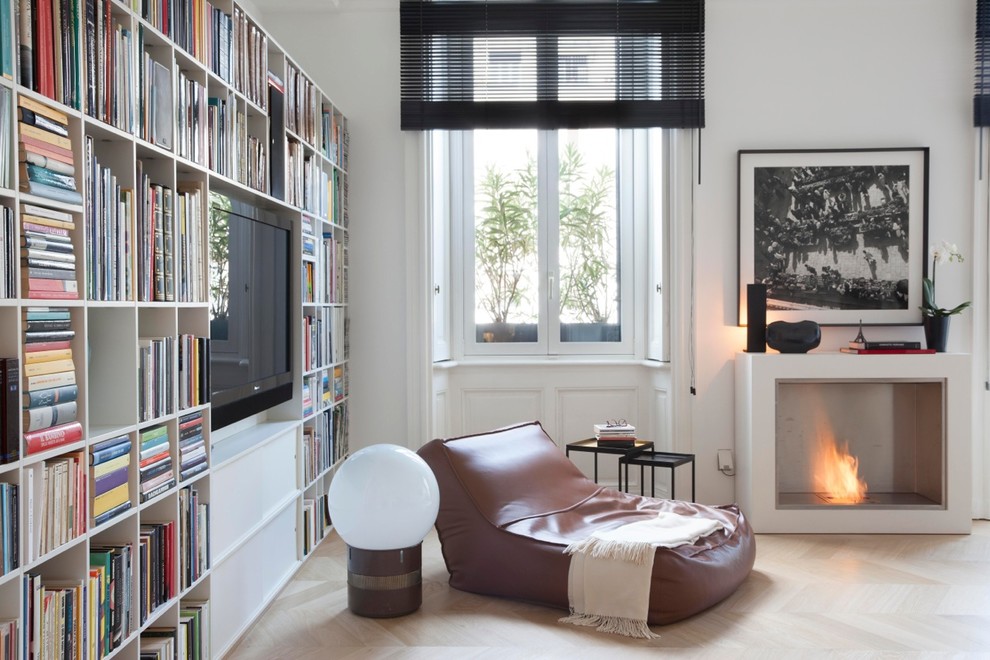Immagine di un soggiorno minimal di medie dimensioni e aperto con libreria, pareti bianche, parquet chiaro, TV a parete e pavimento marrone