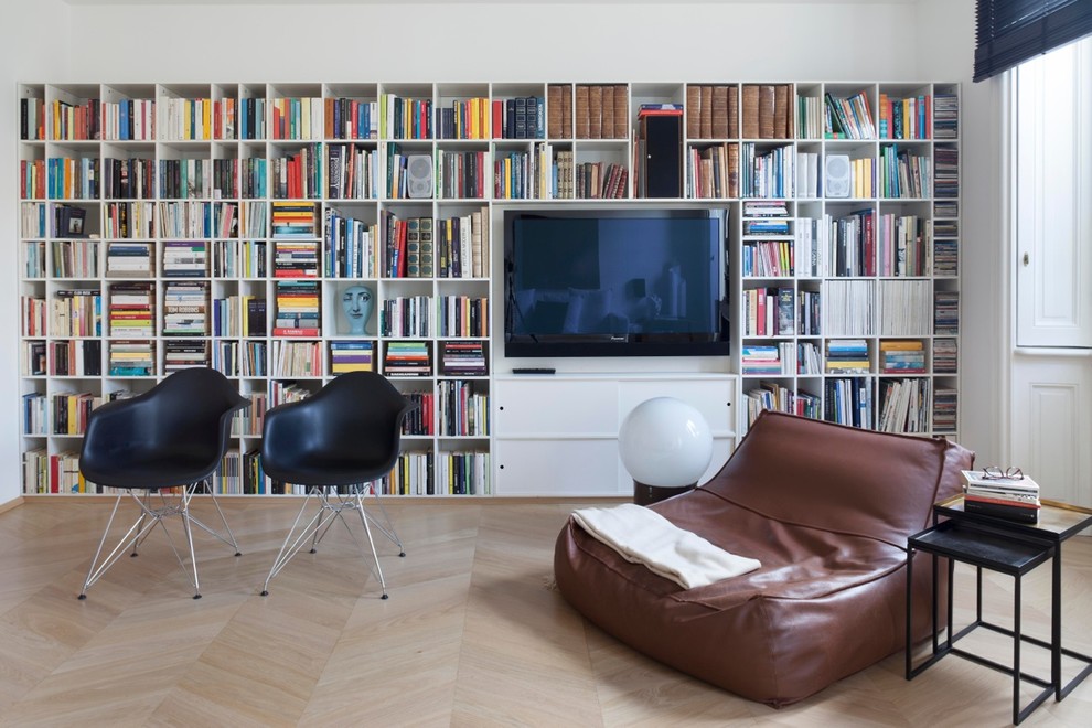 Foto på ett mellanstort funkis allrum med öppen planlösning, med ett bibliotek, vita väggar, ljust trägolv, en väggmonterad TV och brunt golv