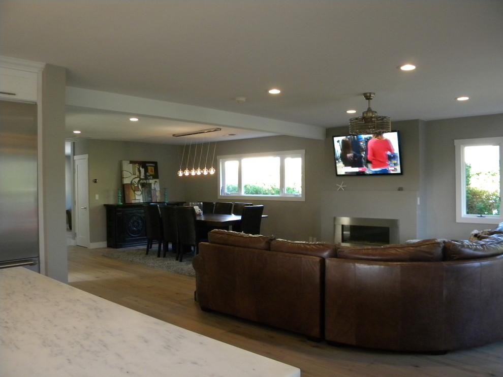 Großes, Offenes Maritimes Wohnzimmer mit grauer Wandfarbe, hellem Holzboden, Kamin, Kaminumrandung aus Metall und TV-Wand in San Diego