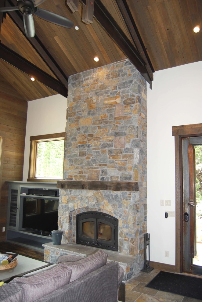 Cette image montre une salle de séjour chalet avec une cheminée standard, un manteau de cheminée en pierre et un téléviseur encastré.