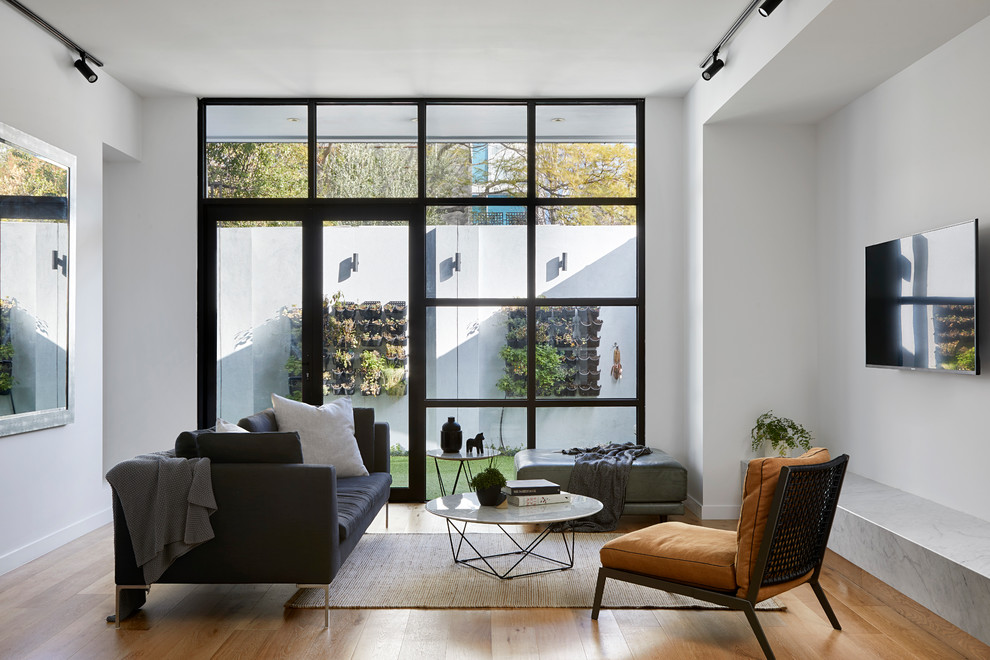 Идея дизайна: гостиная комната в современном стиле с белыми стенами, телевизором на стене, светлым паркетным полом и ковром на полу без камина