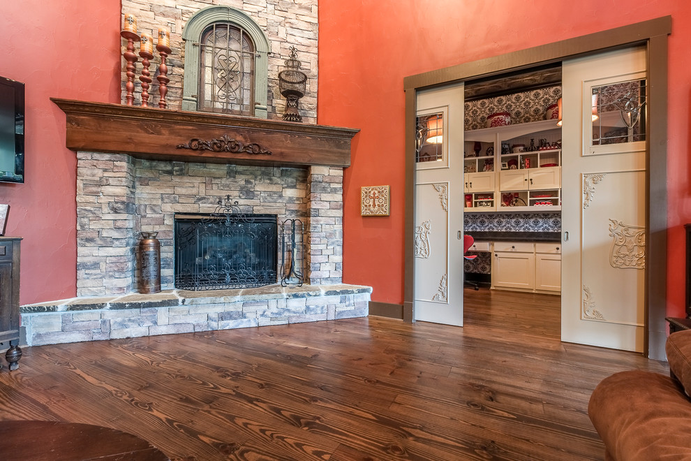 Geräumiges, Offenes Rustikales Wohnzimmer mit roter Wandfarbe, braunem Holzboden, Kamin, Kaminumrandung aus Stein und TV-Wand in Dallas