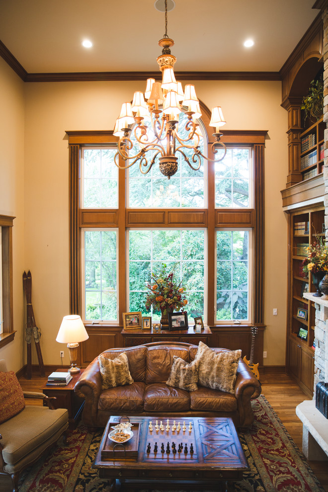 Imagen de sala de estar con biblioteca abierta tradicional extra grande con paredes beige, suelo de madera oscura, todas las chimeneas, marco de chimenea de piedra y televisor retractable