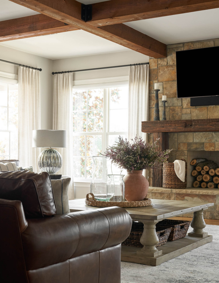 Idée de décoration pour une grande salle de séjour champêtre ouverte avec un mur gris, un sol en bois brun, une cheminée standard, un manteau de cheminée en pierre, un téléviseur fixé au mur et un sol marron.