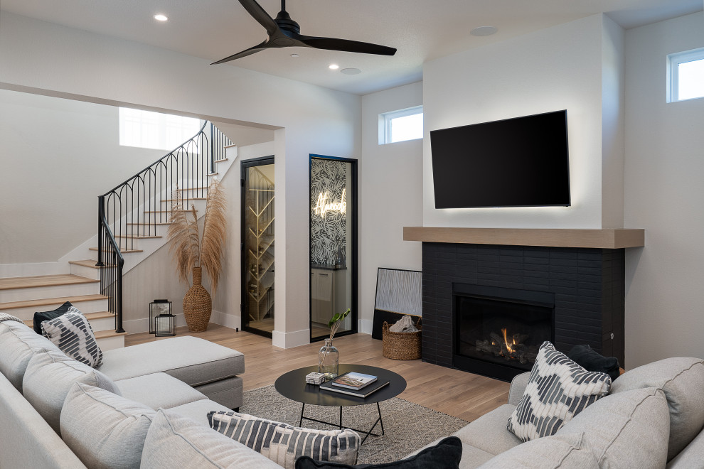 На фото: открытая гостиная комната в стиле неоклассика (современная классика) с белыми стенами, светлым паркетным полом, стандартным камином и телевизором на стене
